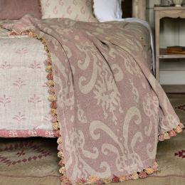 elegant dusky pink linen throw with an Usbek style print and a tassel trim, draped over the edge of a bed. 