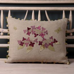 Intricate petals and leaves in shades of purple and green appliqued on to a linen cushion with a pom pom trim. 