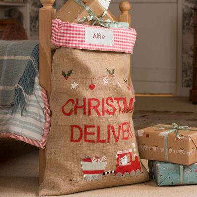 Personalised jute Christmas Sack embroidered with the words 'Christmas Delivery' and Father Christmas driving a train with a carriage of presents. 